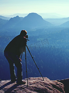 导游和摄影爱好者拿着三脚架站在悬崖上思考。