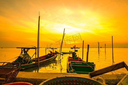 泰国日落时，渔民的船漂浮在竹竿附近的海中。