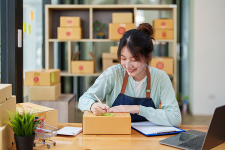 一家小型初创公司和中小企业主（一位亚洲女性企业家）的肖像，正在记事本上写下信息以整理产品，然后将其装入内盒中供客户使用