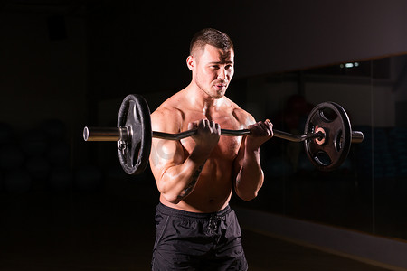 内裤男模腹肌写真摄影照片_肌肉男在健身房锻炼，用杠铃锻炼二头肌，强壮的男性赤裸躯干腹肌