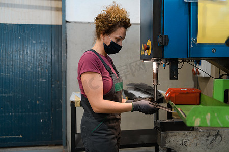 在现代金属工业工作并使用钻头时，因冠状病毒大流行而戴口罩的妇女