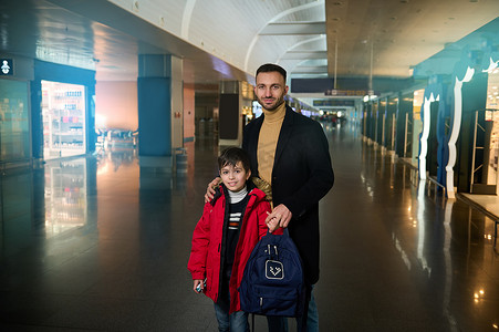 英俊的白人男子，年轻的父亲与十几岁的儿子一起旅行，一起站在国际机场出发航站楼的免税购物区