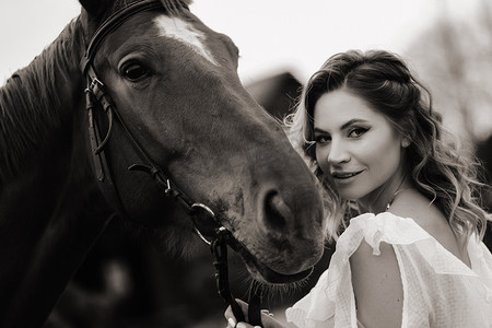 美丽的女孩穿着白色的太阳裙，旁边是一个老牧场的一匹马。