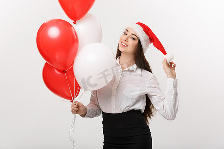 经营理念-美丽的年轻自信的女商人，戴着拿着气球的圣诞老人帽子庆祝圣诞节。