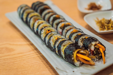 被咬一口汤圆摄影照片_紫菜包饭 (Gimbap) 或紫菜包饭 (Kimbap) 是一种韩国菜肴，由蒸白米包和各种其他配料制成，卷在干紫菜海藻片中，切成一口大小的片。
