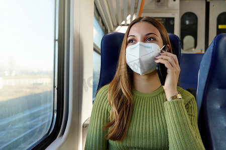 乘坐公共交通需要戴防护面具的年轻女商人坐在火车上打电话