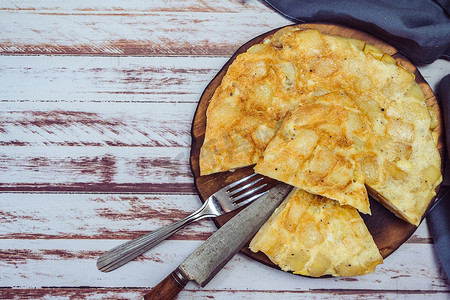 一个盘子的顶视图，上面有西班牙土豆煎蛋卷，在一张木制的乡村桌子上切成八分之一。