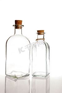 玻璃瓶背光摄影照片_白色背景上带软木塞的两个玻璃瓶，带反射