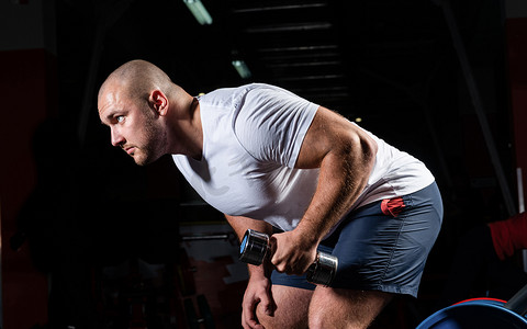 健美运动员摄影照片_男性健美运动员在健身房里用哑铃进行锻炼