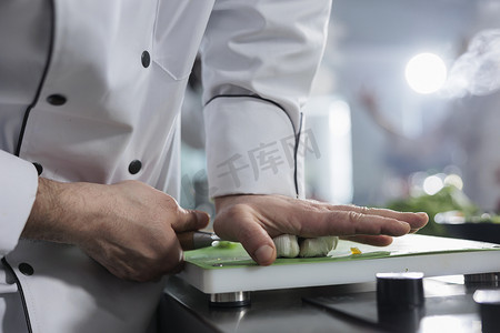 美食专家手的特写，在餐厅专业厨房里用大刀砸碎新鲜大蒜头。