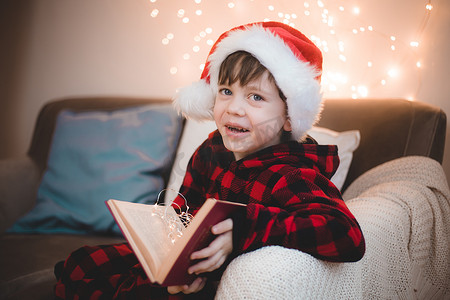 一个戴着圣诞帽的男孩正在生活方式沙发上看书。