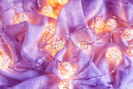 织物褶皱摄影照片_织物褶皱上带有球灯的花环背景 i
