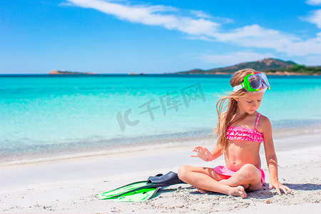 带脚蹼和护目镜的小女孩在海滩上浮潜