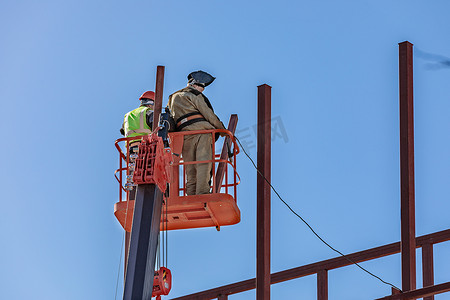 男性建筑工人在升降摇篮中高空作业，建造建筑物的铁框架