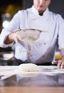 厨师面团摄影照片_厨师在新鲜的披萨面团上撒上面粉