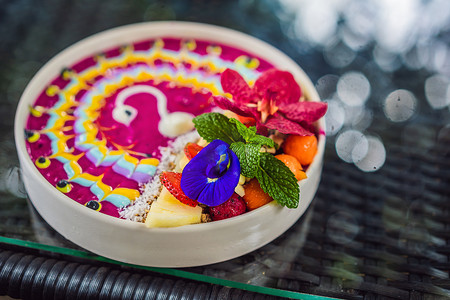 健康的热带早餐，冰沙碗配有热带水果，装饰着彩色酸奶图案，配有姜黄和螺旋藻。