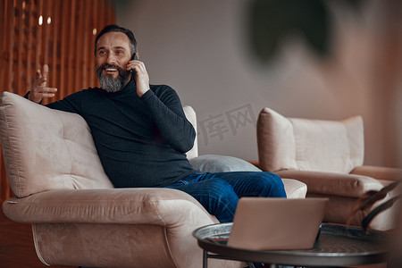 微笑的留着胡子的男人坐在扶手椅上打电话聊天