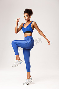 全长坚定的健身女孩穿着蓝色运动服在健身房锻炼，看上去很严肃，站在白色背景上