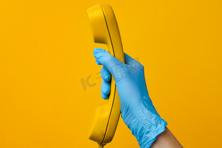 老式扬声器摄影照片_戴着医用手套的女手拿着黄色电话扬声器
