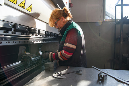 机床摄影照片_在现代化工厂工作并为数控机床准备材料的妇女。