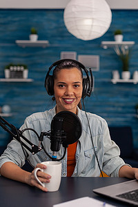女视频博主拿着杯子和使用笔记本电脑播放播客的肖像。