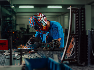专业重工业焊工在工厂内工作，戴着头盔并开始焊接。