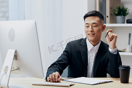 穿着西装、喝着咖啡的男人坐在电脑前的桌子旁