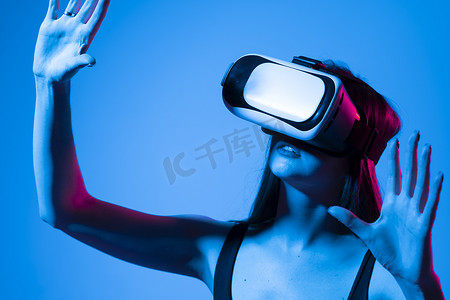 年轻女子戴着 VR 眼镜站在工作室里，用手在虚拟空间中滑动滚动缩放，同时与虚拟宇宙中的物体进行交互。
