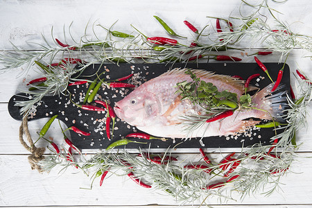 生鲜粉色罗非鱼鱼躺在撒有小红辣椒的板上
