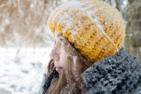一位微笑的年轻白人女子的肖像，戴着明亮的羊毛帽子和围巾，背景是白雪皑皑的森林。