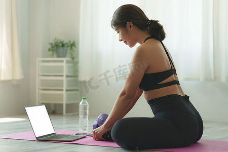 在线课摄影照片_年轻女子在家练习瑜伽，跟随老师在笔记本电脑在线课堂上练习。