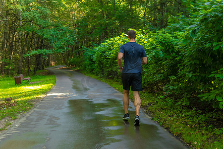 一名男子运动员在公园户外跑步，周围是森林、橡树绿草、年轻持久的运动运动员跑步健身户外适合双腿男性，外面有树木。