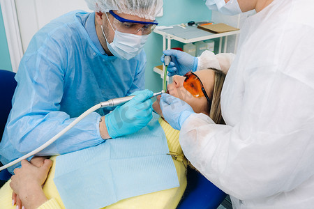 一名男牙医带着牙科工具和助手一起给病人钻牙。