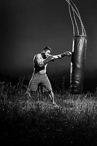 体育锻炼黑白摄影照片_一名男拳击手用沙袋训练的单色照片