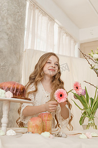 一个穿着浅色连衣裙、长发的女孩坐在复活节餐桌旁，桌上摆着蛋糕、春天的花朵和鹌鹑蛋。