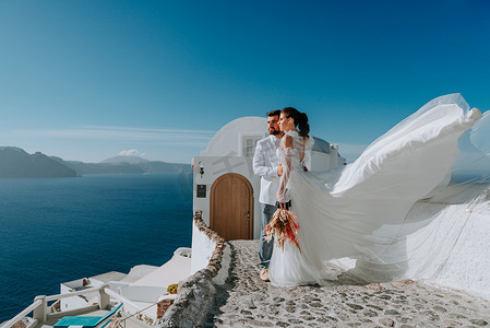 希腊圣托里尼岛摄影照片_美丽的新娘和新郎在希腊圣托里尼岛的夏季婚礼上