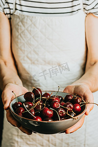 一碗西瓜摄影照片_老女服务员在盘子里提供并拿着一串樱桃，水果，健康生活，良好的饮食，地中海概念，复制空间，垂直图像