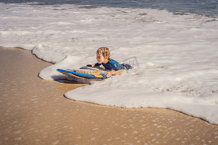 快乐的小男孩在度假时在海滩上玩得开心，带着布吉板
