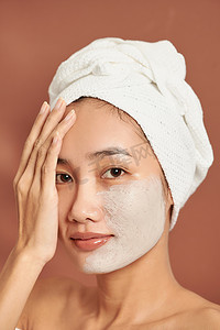 一个漂亮的年轻亚洲女孩头上戴着白毛巾，脸上贴着有用的粘土面膜