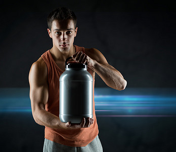 健美运动员摄影照片_年轻男性健美运动员拿着装有蛋白质的罐子