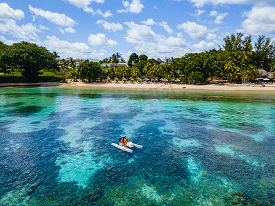 田园诗般的棕榈树环绕的海滩上的桨板和脚踏船，一对男女在毛里求斯度假