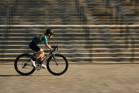 职业女自行车手穿着自行车服和防护装备在城市骑自行车、白天在户外训练时冲过建筑物的侧视图