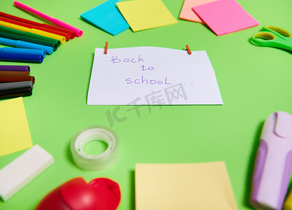 重点关注一张白纸，上面写着“回到学校”，中心是各种颜色的文具办公用品和学校配件，排列成圆圈。