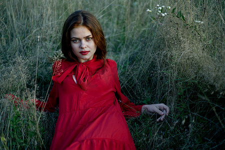 穿着红色连衣裙风景时尚的女人躺在草地上