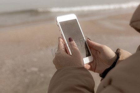 美丽的女人在海滩上使用智能手机