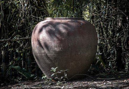 风采园地摄影照片_旧的大土罐或大型老式粘土罐，用于花园地面上的储水，有许多绿树自然。