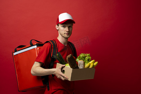 身穿红色制服的送货员拿着工艺纸板箱，里面装着白色背景、工作室肖像中隔离的食物。
