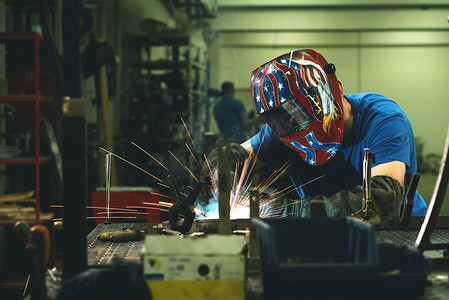 专业重工业焊工在工厂内工作，戴着头盔并开始焊接。