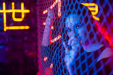 霓虹灯网格摄影照片_霓虹灯工作室里链环网后面的白人妇女。