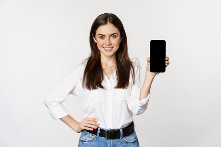 app展示界面摄影照片_穿着公司服装的自信女性，展示智能手机屏幕、应用程序的移动界面，站在白色背景上